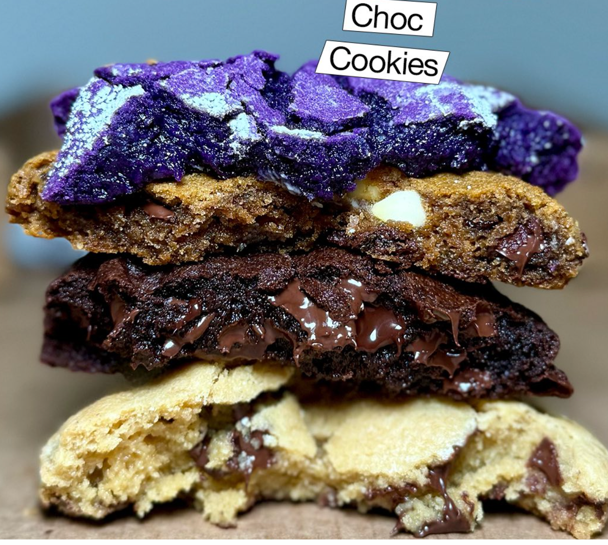 CHOC Cookies' signature four-cookie stack featuring vibrant purple Ube, rich Cookies & Creme with Oreo pieces, dark chocolate with melted center, and classic chocolate chip cookies split to showcase each unique texture and filling, professional bakery photography